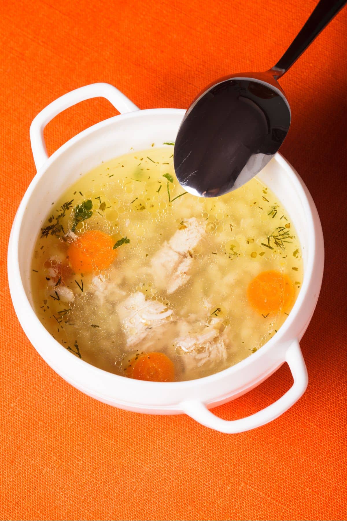 A bowl of chicken broth sitting on a vibrant orange background.