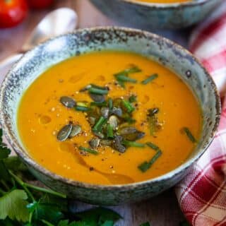 A bowl of delicious velvety butternut and sweet potato soup, garnished with chives and pumpkin seeds.