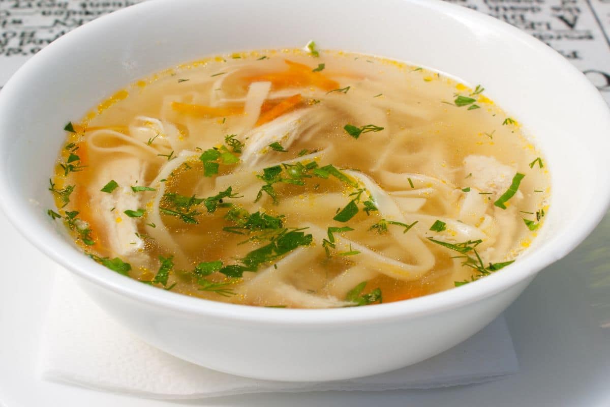 A bowl of chicken noodle soups, with green shredded herbs floating on top.
