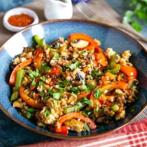 A dish of colourful fried oatmeal with vegetables, garnished with sesame and herbs.