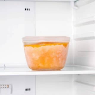 A pot of frozen soup in the freezer. It's an orange, carrot based soup, in a plastic pot.