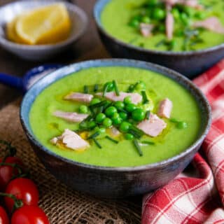 Two bowls of fresh green pea and ham soup, green and vibrant and garnished with peas, chives and ham.