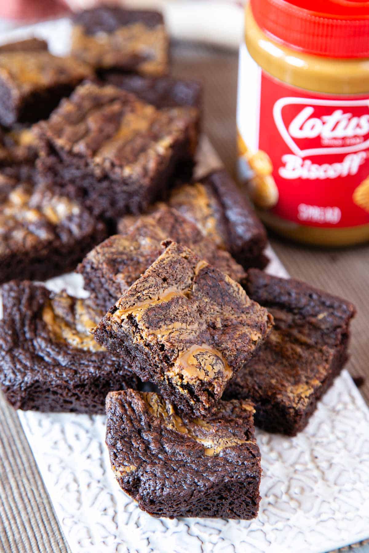 A serving board with rich chocolate brownies swirled with buttery Biscoff spread, and a tub of the spread on the side.