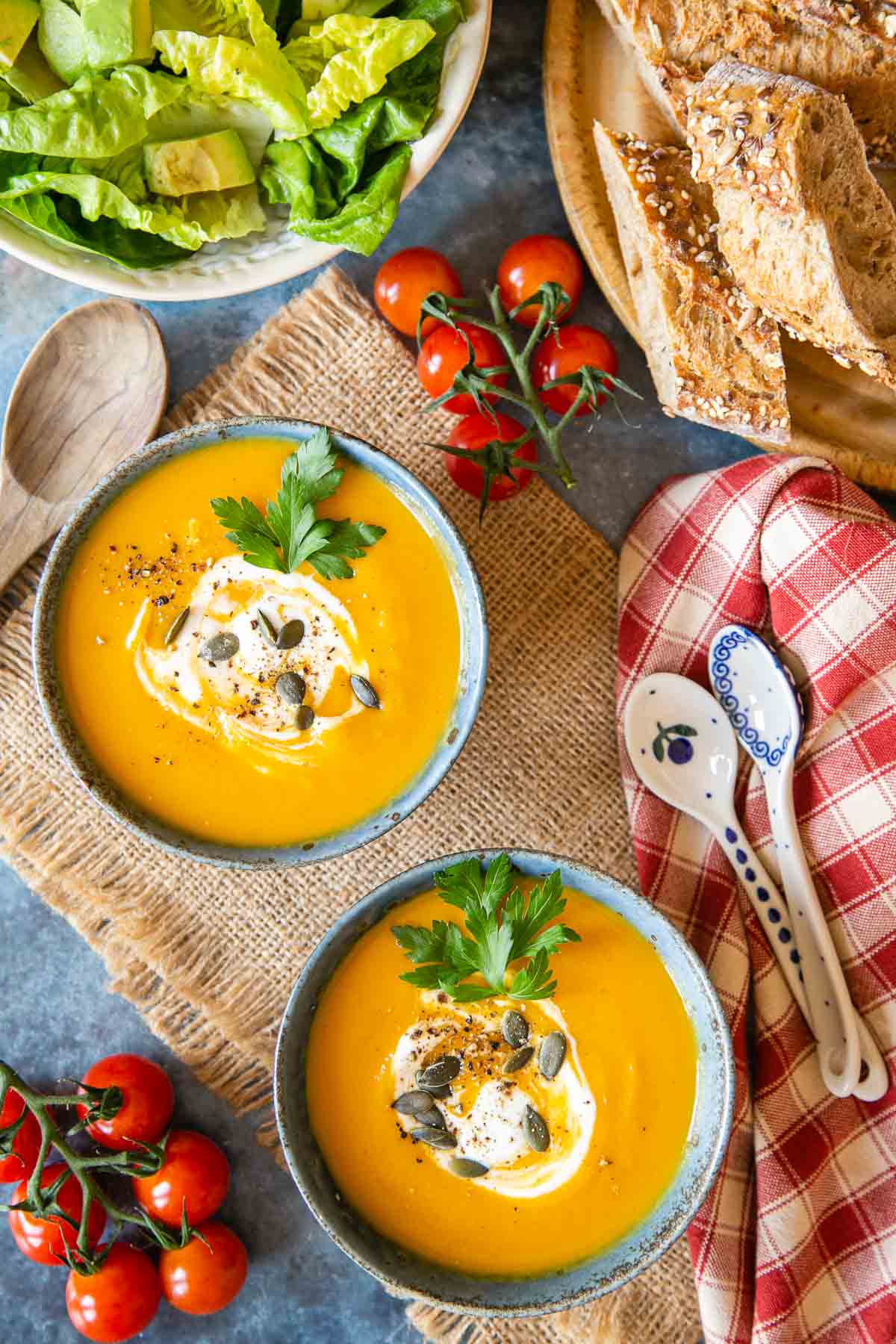 top down view of a table set with two bowls of golden sweet potato and carrot soup, fresh bread, a green salad and vine tomatoes