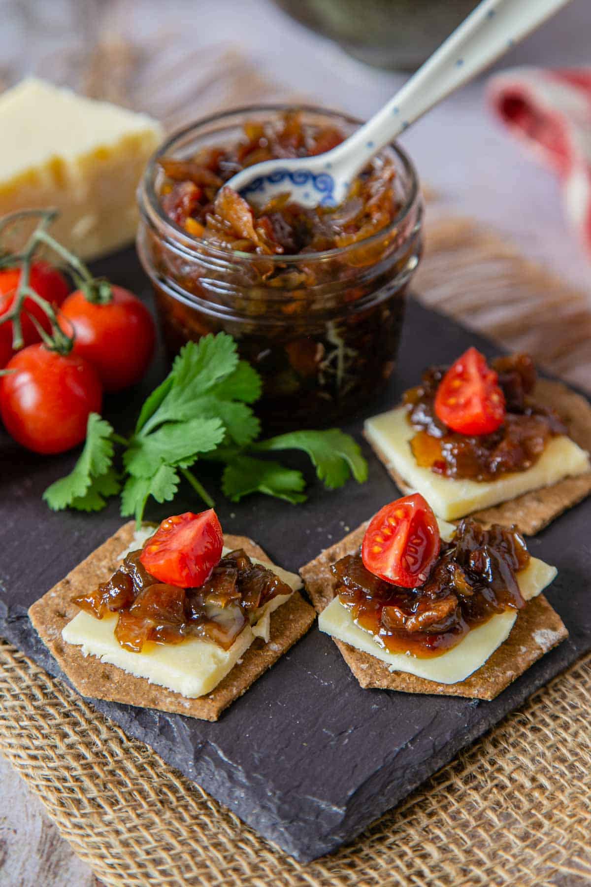 Bourbon bacon jam in a jar and topping cheese and crackers along with cherry tomatoes.