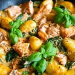 Creamy salmon gnocchi, generous flakes of salmon in a cream and tomato saucce with gnocchi and spinach - a colourful dish, scattered with basil leaves.