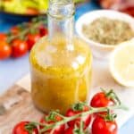 A bottle of Greek dressing, ready to add to a salad. Bright red tomatoes in the foreground.