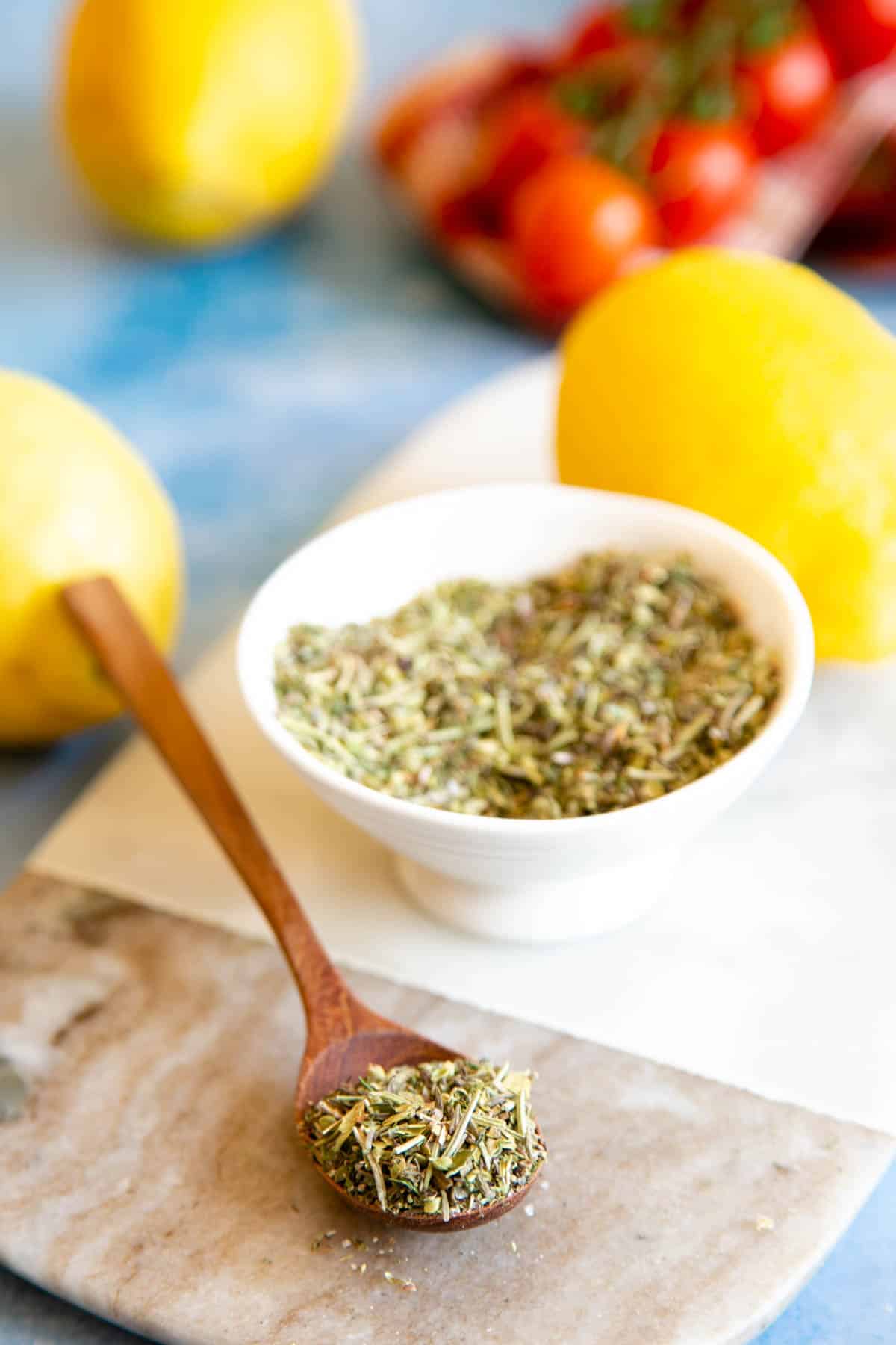 A spoonful of Greek seasoning, resting on a marble board. Bright yellow lemons in the background.