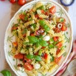 A view of a serving plate of Italian pasta salad, flecked with red, white and green, fresh and juicy with salad vegetables and fresh herbs.