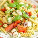 Close up view of Italian pasta salad with red and green peppers, tomatoes, white cheese and vibrant green basil.