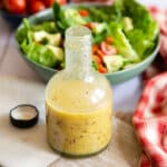 A bottle of sweet and tangy honey mustard dressing next to a fresh green salad.