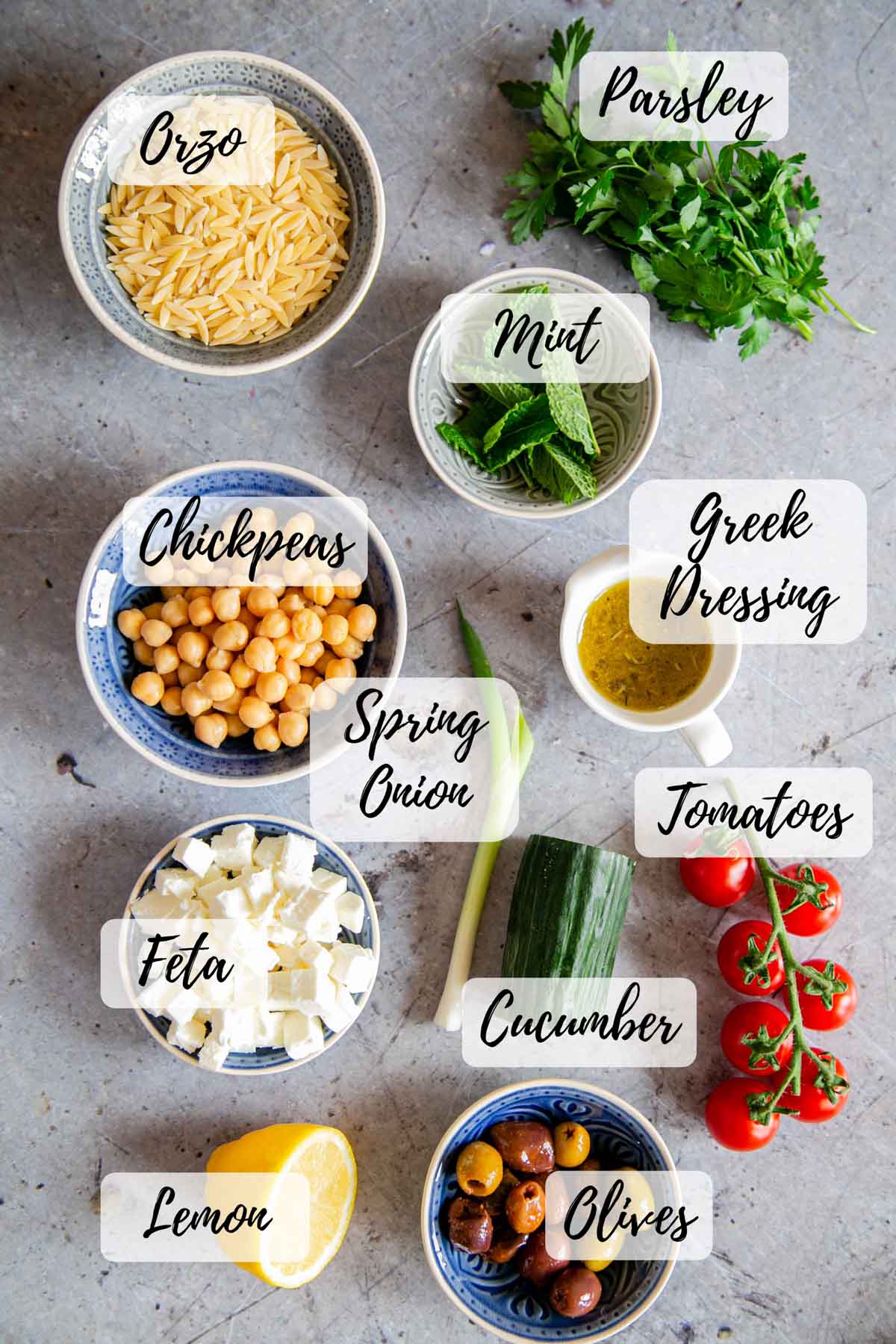 The ingredients, ready to cook: orzo pasta, parsley, mint, Greek salad dressing, cucumber, tomatoes and spring onion, olives, lemon, feta cheese and chickpeas.