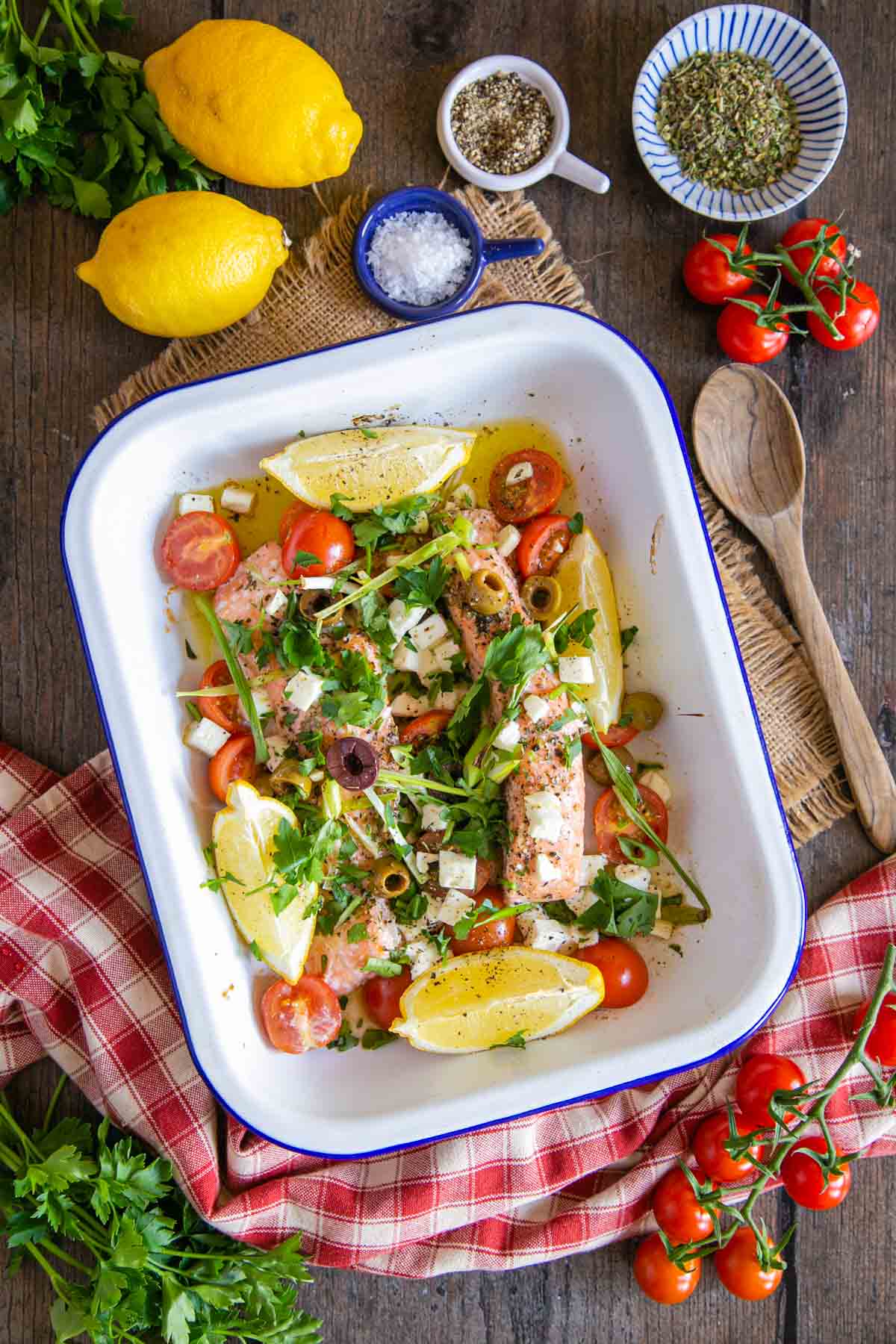 A dish of Greek salmon with feta, vegetables and lemon shown from above on the table, fresh from the oven and ready to serve.