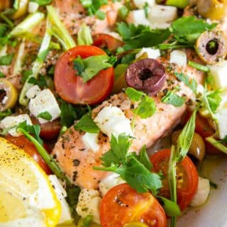 close up of Greek baked salmon, scattered with herbs, feta and vegetables.