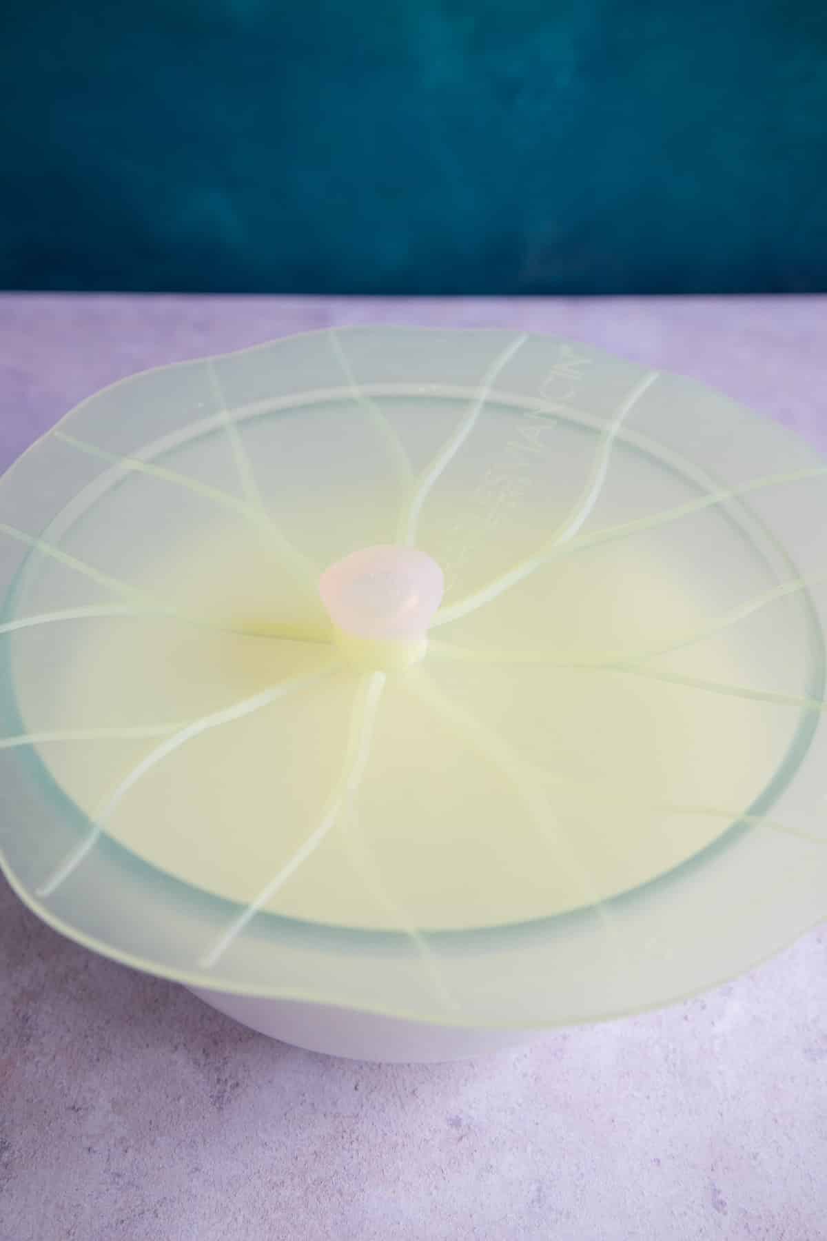 A bowl of kefir grains and milk, covered with a silicone cover.