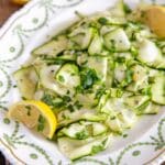 A plate of courgette salad, light and bright courgette ribbons in lemon dressing with lemon wedges.