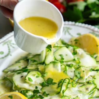 Drizzling lemon dressing over fresh green courgette salad.