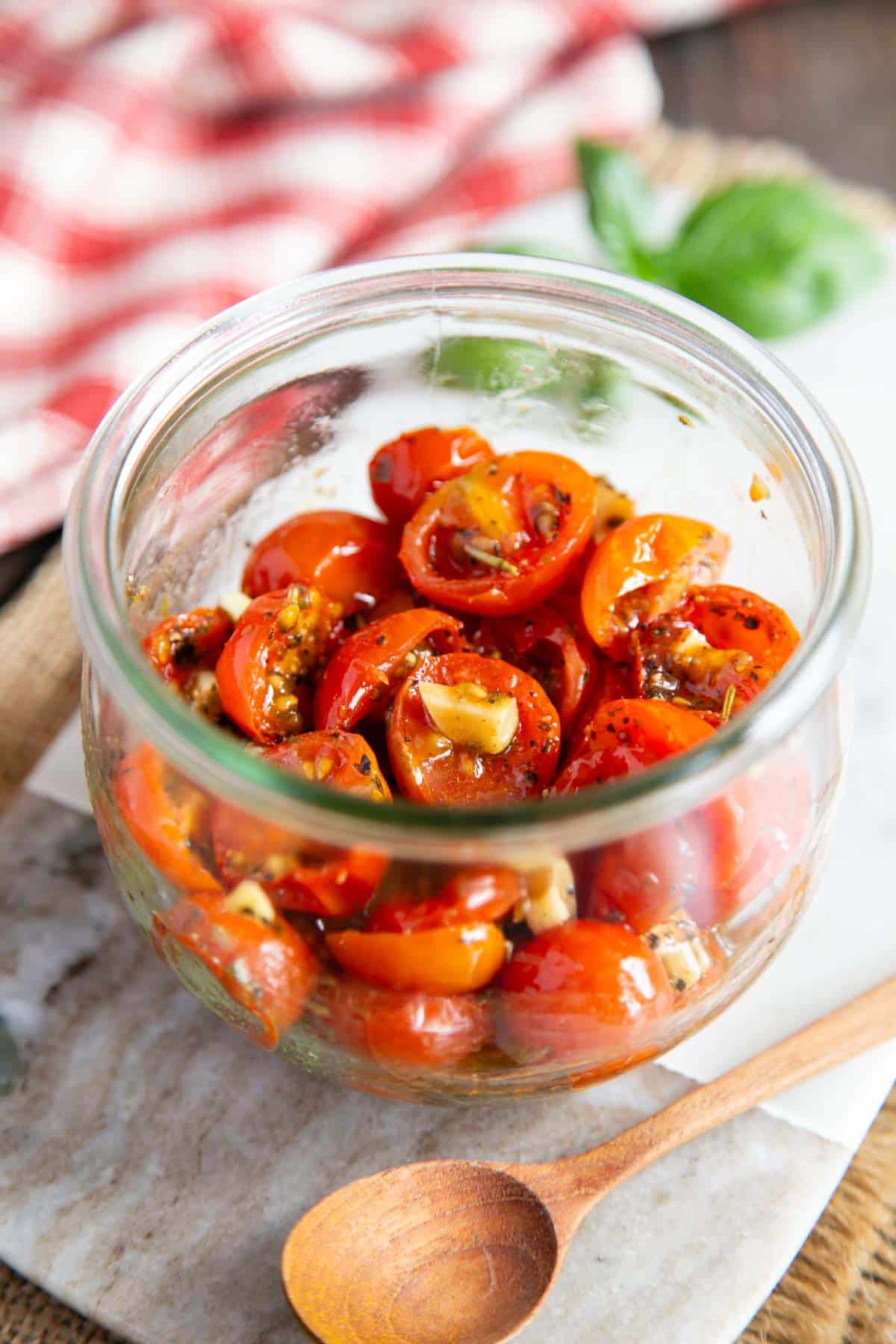 A jar of flavour packed cherry tomatoes on a serving board with a spoon, ready to enjoy.