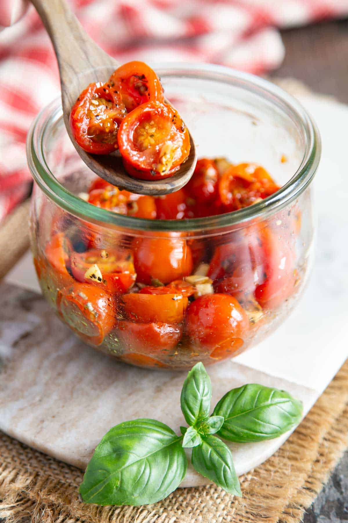 Lifting delicious confit cherry tomatoes from the jar with a spoon.