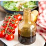 An attractive bottle of rich dark balsamic dressing on a serving board, next to a a vine of red cherry tomatoes.