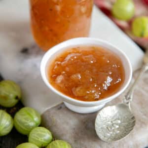 a small bowl of gooseberry jam, surrounded by fresh gooseberries