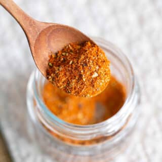 A spoonful of orange paella spice mix in a small wooden spoon, being taken from a jam jar.