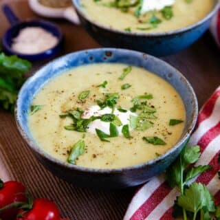 bowls of velvety green broccoli cauliflower soup garnished with cream and herbs
