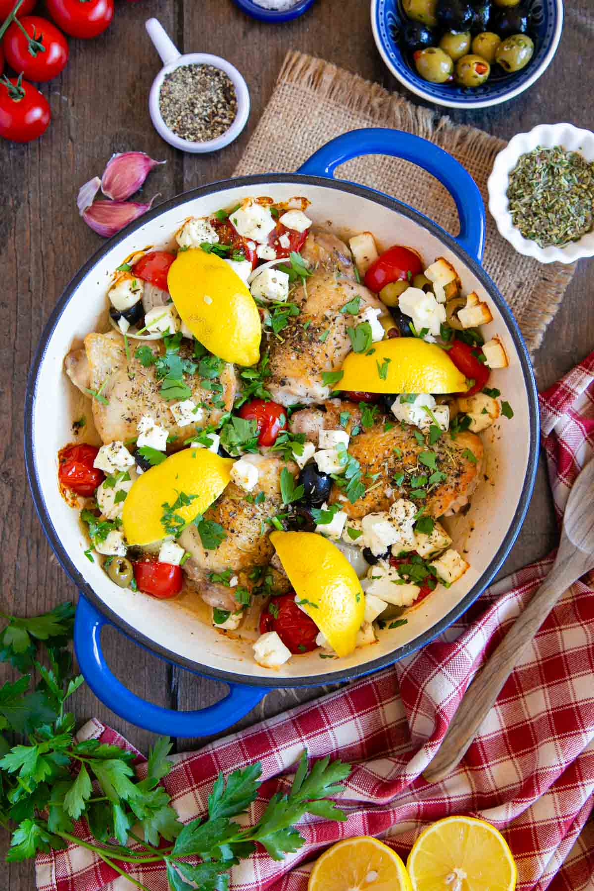 Greek chicken shown from above served up a blue casserole dish that contrasts with the bright colours of the dish.