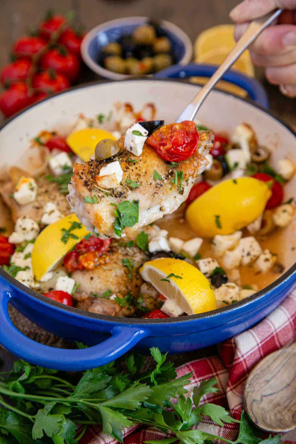 Greek chicken, a burst of colour with lemons, tomatoes, white feta and green herbs all contrasting with the bright blue of the casserole dish.