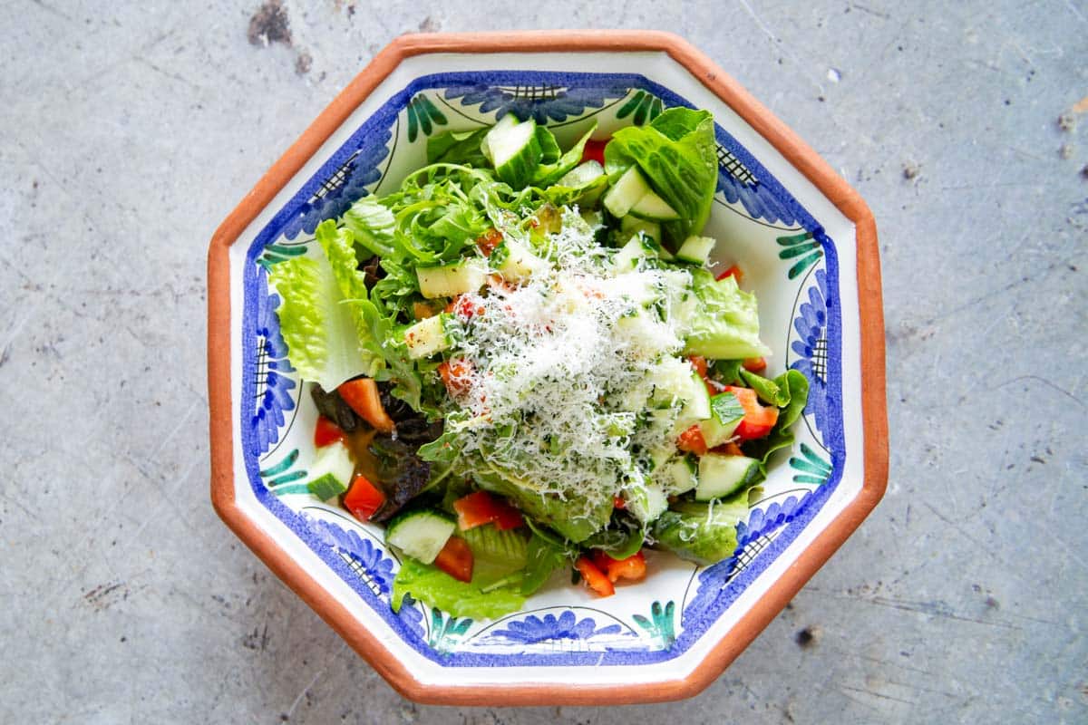 The parmesan cheese grated over the salad leaves, cucumber and pepper in a serving dish.