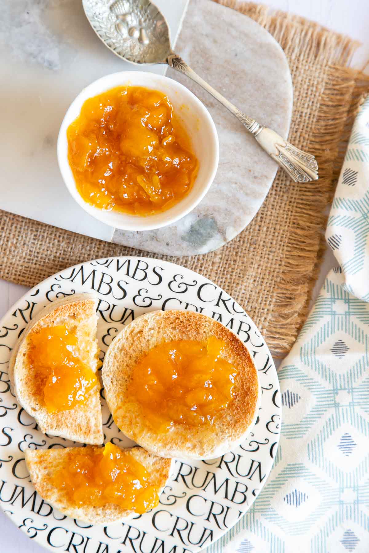 Mango jam on muffins, with a dish of mango jam and a fancy silver spoon, shown from above.