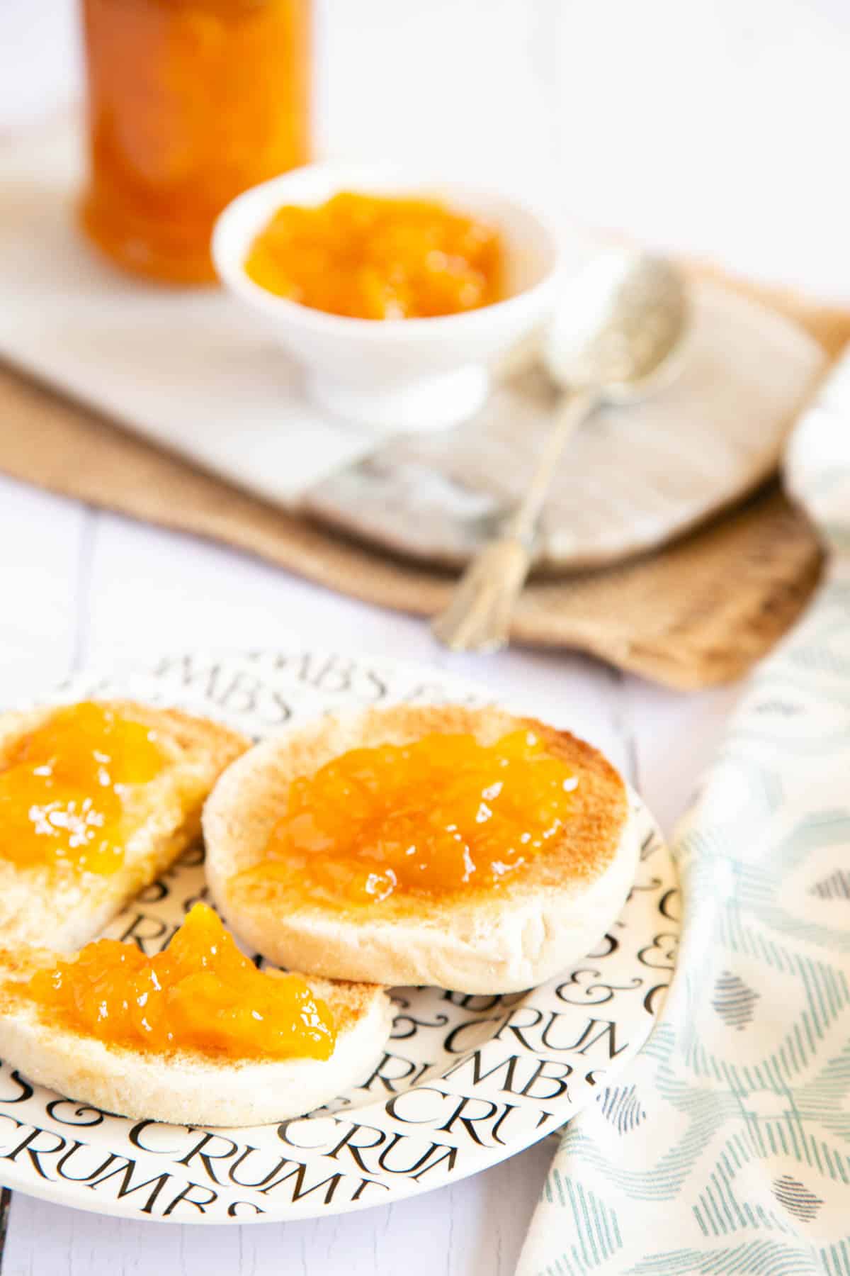 Delicious muffins spread with golden mango jam, a serving board in the background with a jar and a dish of jam.