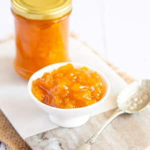 Golden mango jam in a jar and in a dainty serving dish, with a silver spoon alongside.