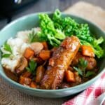 Slow cooker sausage casserole served in a bowl with mashed potato and savoy cabbage, the slow cooker in the background.