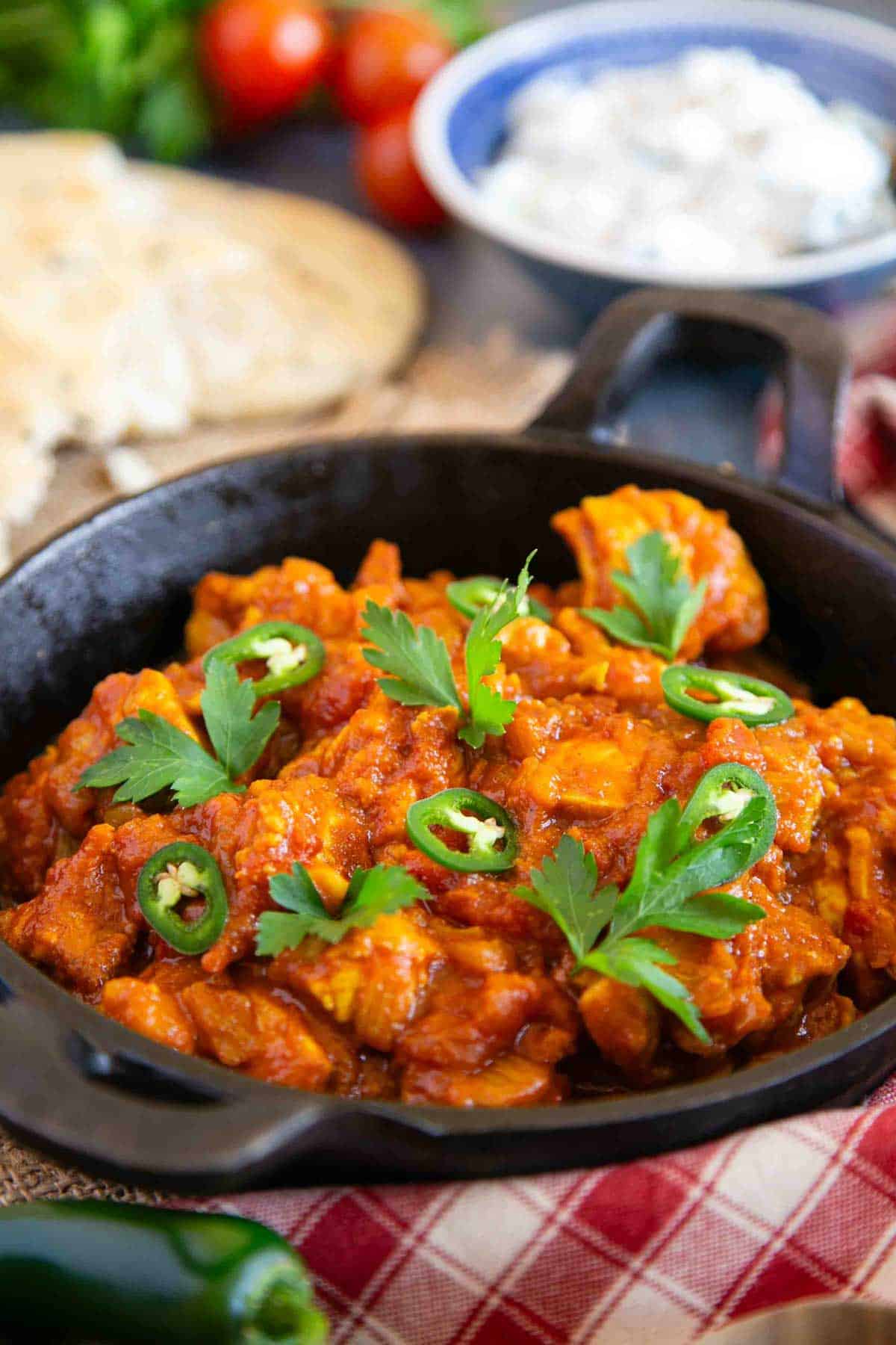 Close up view of chicken bhuna in the serving dish, garnished with sliced finger chillies and fresh coriander.