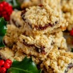 meltingly delicious mincemeat crumble bars, piled up on a serving plate, surrounded by Christmas holly.