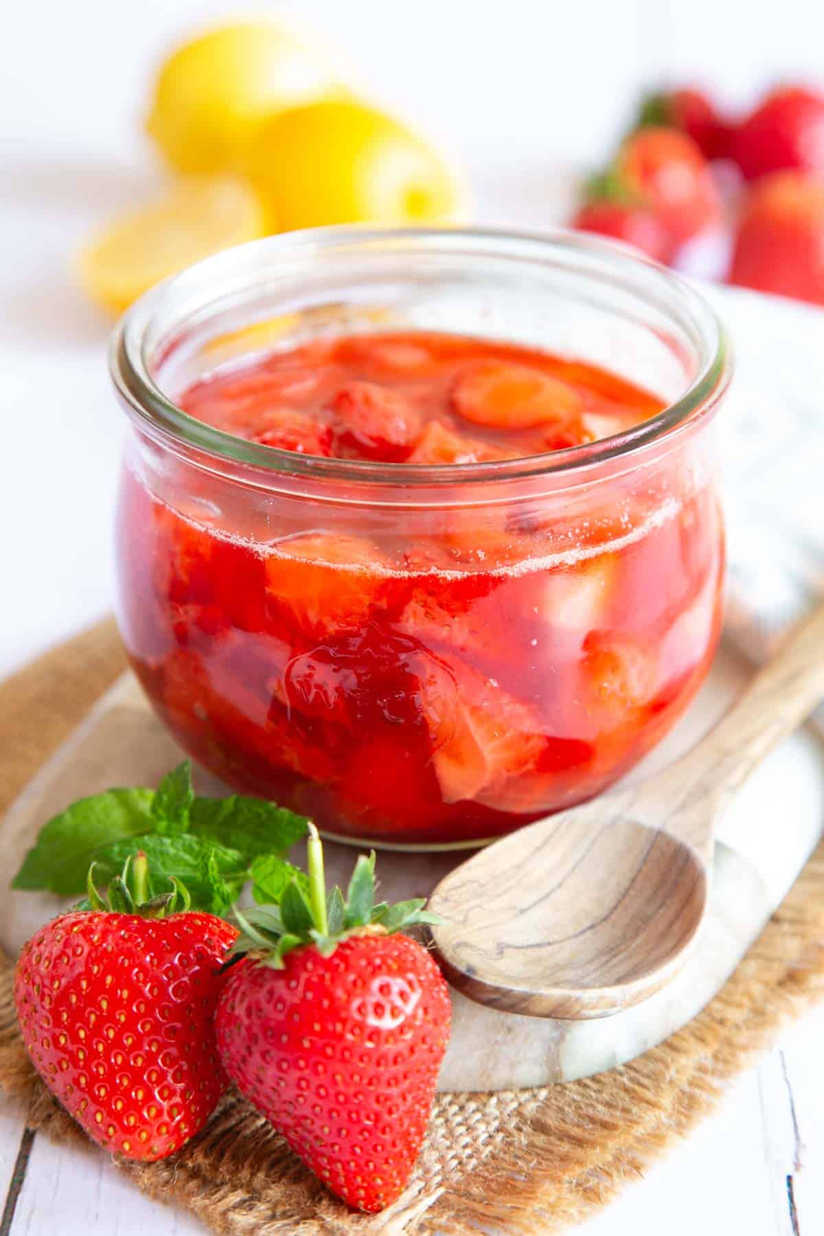 Strawberry compote in a glass jar, the fruit clearly visible floating in a rich syrup.