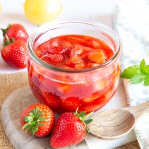Strawberry compote in a glass jar, the fruit clearly visible floating in a rich syrup.