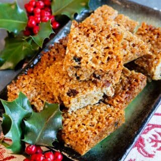 A pile of golden, buttery mincemeat flapjacks on a green glazed platter surrounded by holly.