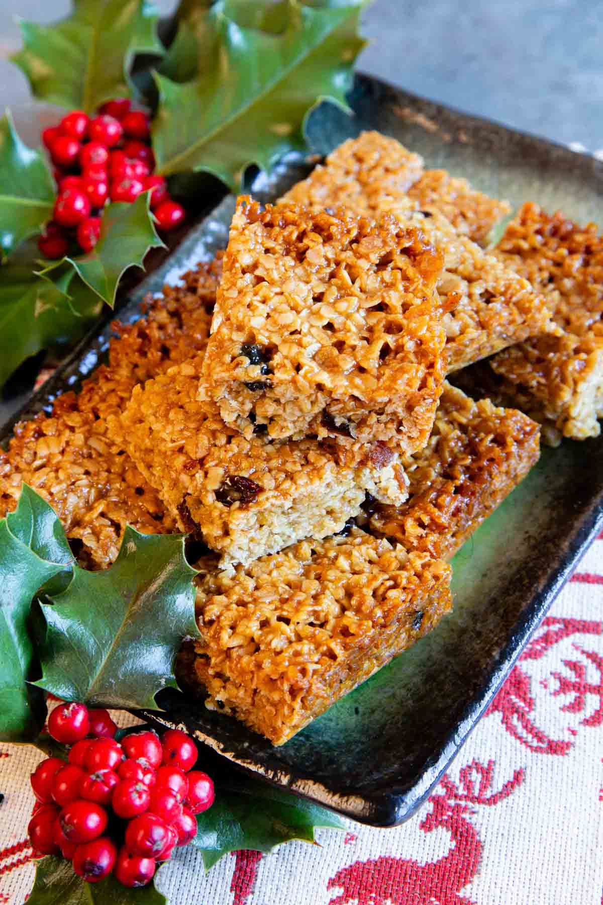 A pile of golden, buttery mincemeat flapjacks on a green glazed platter surrounded by holly.