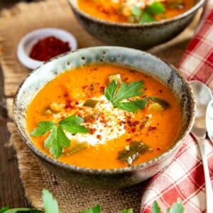 A bowl of pinto bean soup garnished with sour cream, coriander leaf and chilli