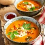 Bowls of pinto bean soup garnished with sour cream, coriander leaf and chilli and photographed against a colourful checked cloth.