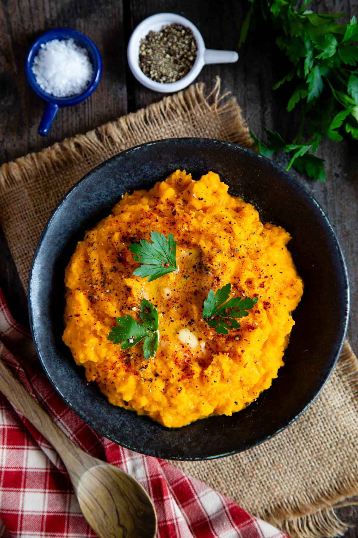 Carrot and swede mash, a delicious golden orange vegetable side, vibrant against a dark serving bowl and garnished with parsley.