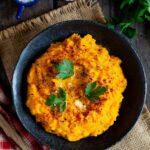 Golden carrot and swede mash, vibrant against a dark serving bowl and garnished with parsley.
