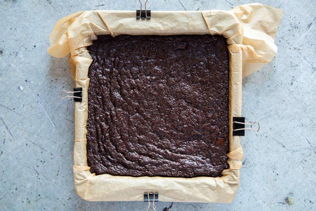 The baked brownie has sa slightly wrinkled, papery crust and has pulled away from the edges of the pan.