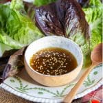 A bowl of miso dressing topped with black and white sesame seeds, served with crisp lettuce leaves.