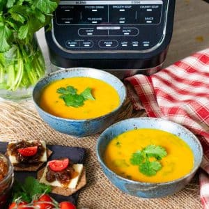 Two bowls of carrot and coriander soup next to the soup maker, with crackers and cheese on the side.
