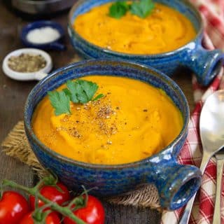 Two blue bowls of golden orange carrot and lentil soup on a table ready to be enjoyed