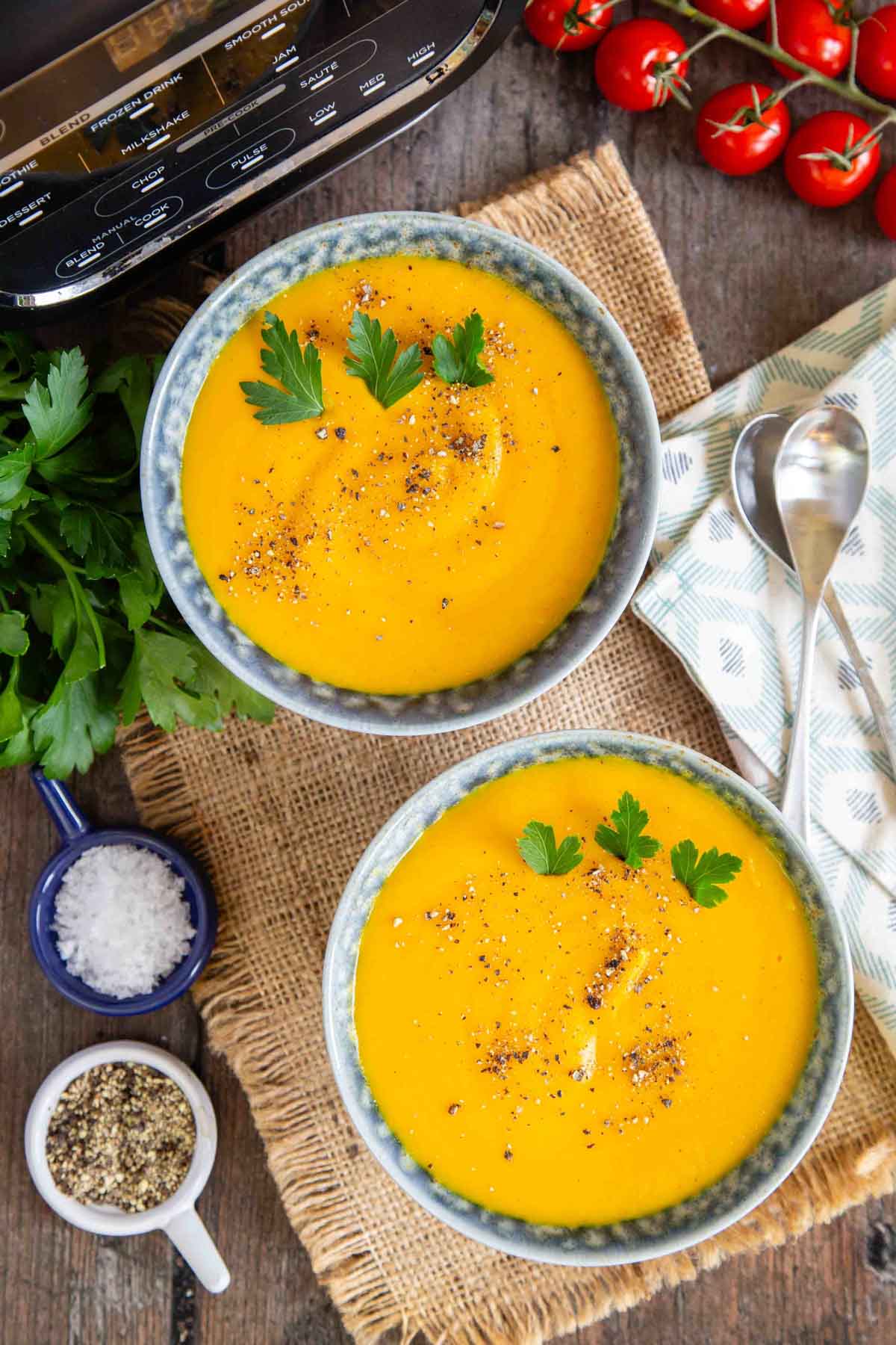 Two bowls of deep yellow carrot and parsnip soup on a table top ready to eat