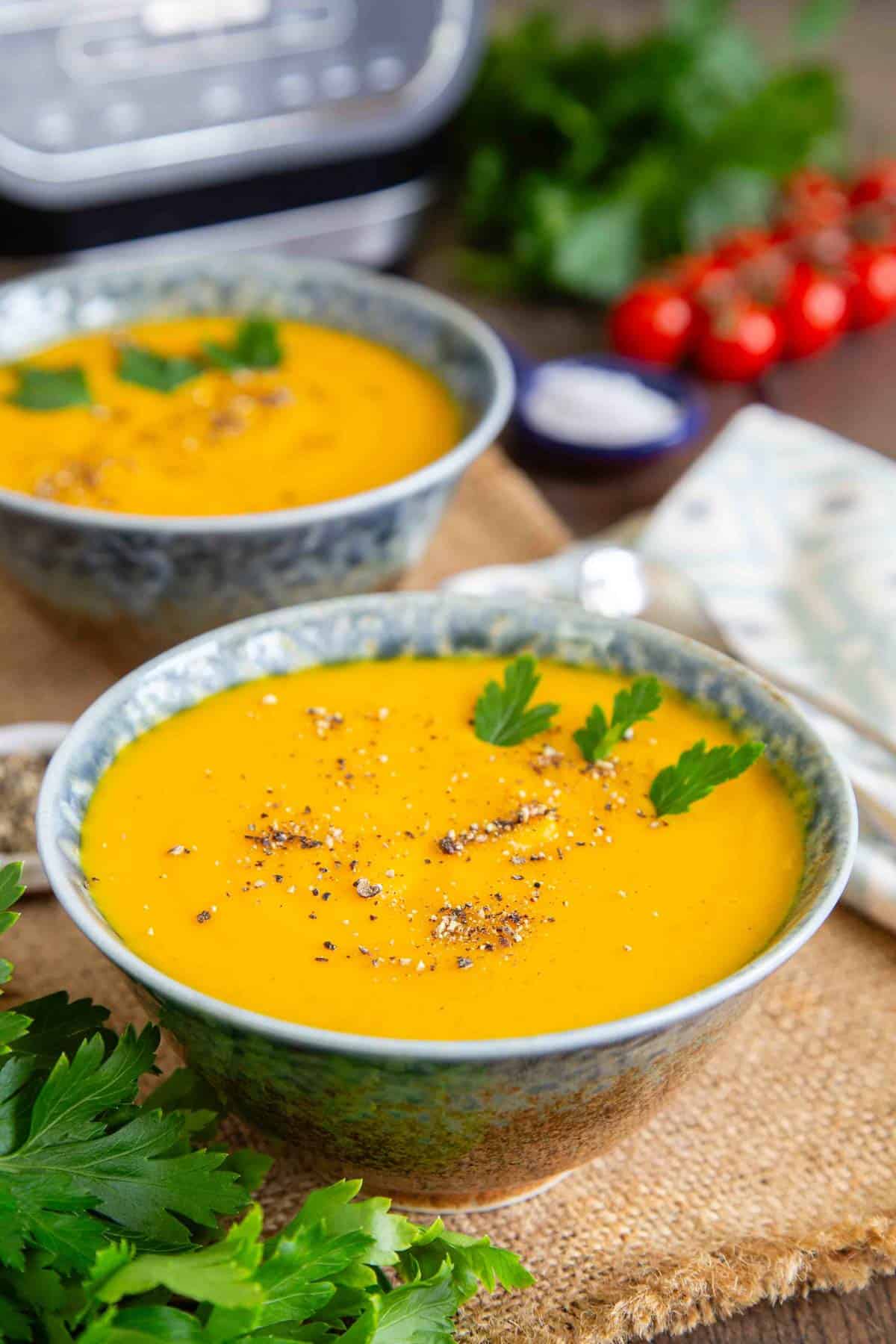 Two bowls of deep yellow carrot and parsnip soup on a table top ready to eat